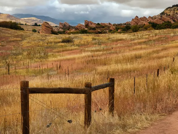 Red rocks formation with golden prairie and fence post foreground