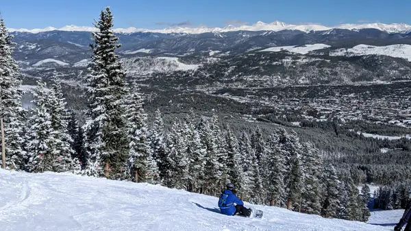 Skier resting on Breckenridge slope with town and mountains below