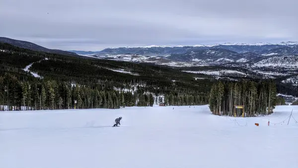 Lone snowboarder on wide open run with valley and forest below
